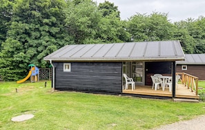 A small cabin with a porch, a slide, and a deck with chairs.