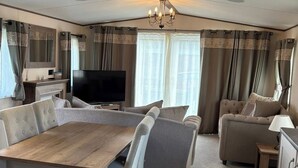 Ein geräumiger Wohnbereich mit Esstisch aus Holz, Sofas, einem Fernseher und Vorhängen.