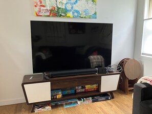 Ein Wohnzimmer mit einem großen Flachbildfernseher, einer Holz-Unterhaltungseinheit und einem Bücherregal mit Gesellschaftsspielen.
