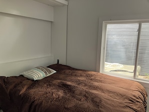 Ein Schlafzimmer mit einem Bett, einem Fenster mit Jalousien und einer Wandleuchte.
