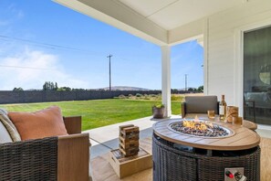 En overdækket terrasse med bålsted, fletningsmøbler og udsigt over en græsplæne.