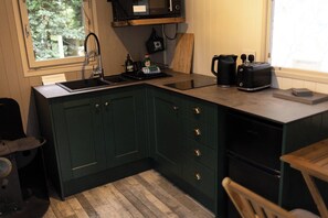 A kitchen with dark green cabinets, a black countertop, a sink, and a window with a view of trees. - Shepherd's Hut - Sleeps 2 - Hot Tub (Northwich)