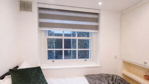 A bedroom with a window, a bed with pillows, a bedside table, and a shelf with a bowl. - 6 Bed House Sleeps 16 - Central London, Parking (London)