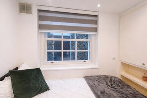 A bedroom with a window, a bed with pillows, a bedside table, and a shelf with a bowl. - 6 Bed House Sleeps 16 - Central London, Parking (London)
