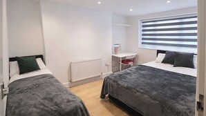 A bedroom with two beds, a radiator, a desk with a chair, and a window with blinds. - 6 Bed House Sleeps 16 - Central London, Parking (London)