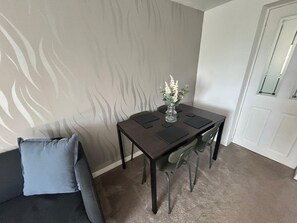 Ein Essbereich mit Tisch, Stühlen, einer Blumenvase und einem grauen Sofa.
