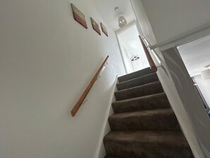 A carpeted staircase with a wooden handrail, white walls, and a door at the top.