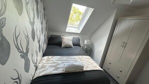 Ett sovrum med en säng, ett fönster, en garderob och tapeter med ett mönster.