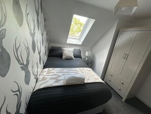 Ein Schlafzimmer mit Bett, Fenster, Kleiderschrank und strukturierten Tapeten.
