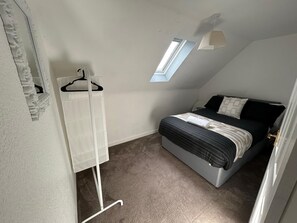 A bedroom with a bed, a hanging clothes rack, a skylight, and a door.