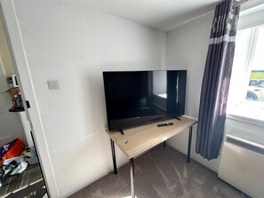A room with a flat-screen TV on a wooden stand, a window with curtains, and a radiator.
