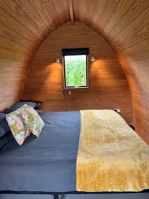 A cozy, wooden-paneled room with a bed, pillows, and a window.