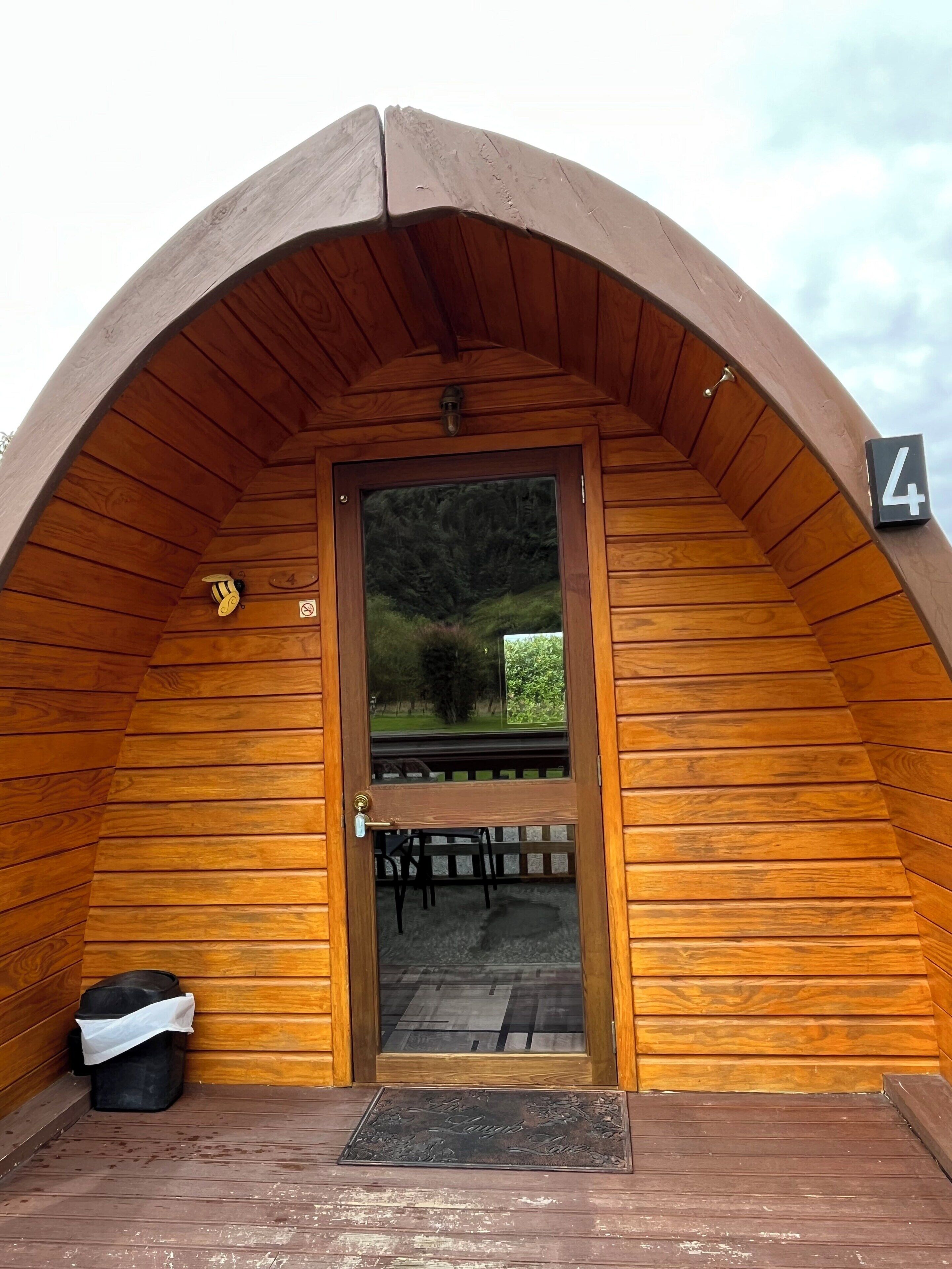 A wooden cabin with a curved roof, a door with a number plate, and a bench outside.