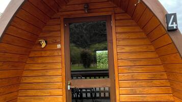 A wooden cabin with a curved roof, a door with a number plate, and a bench outside.