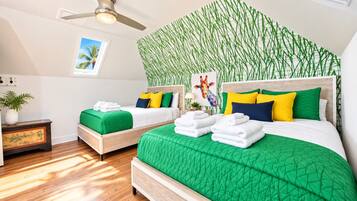 A hotel room with two beds, a ceiling fan, a wall with a green plant mural, and a small table with a plant.