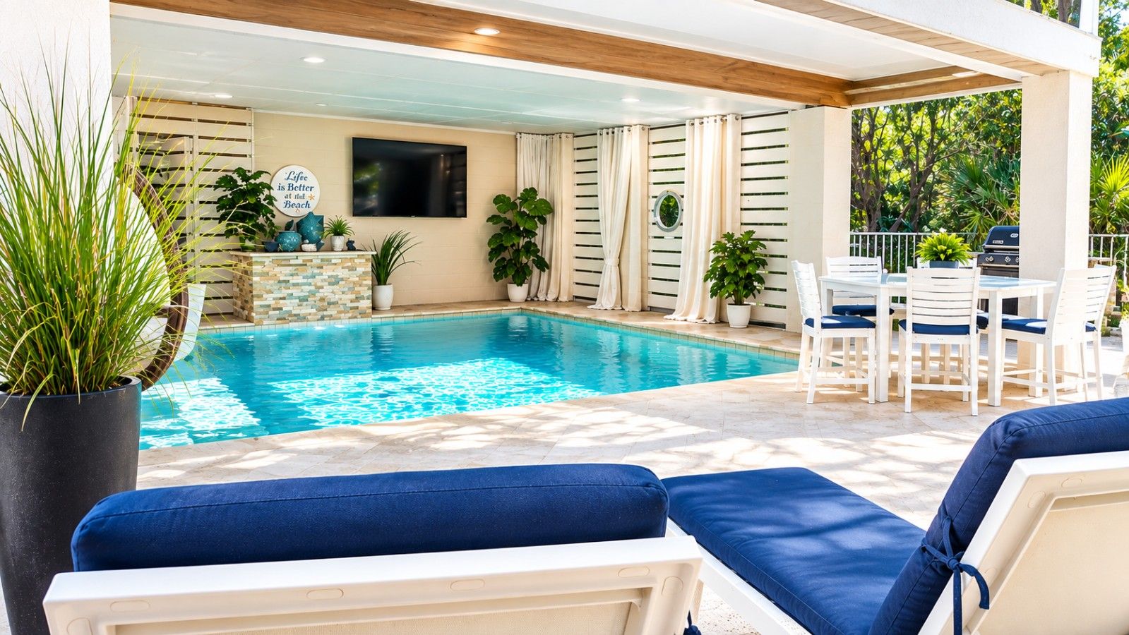 A poolside area with lounge chairs, a table, and potted plants.