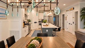 Una cocina moderna con una isla central, iluminación colgante y una zona de comedor con mesa y sillas de madera.