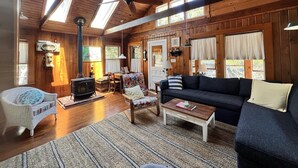 Un acogedor interior de cabaña con chimenea, paredes de madera, un sofá, una mecedora y un comedor.