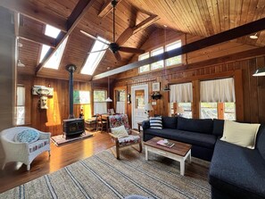 Ein gemütliches Blockhäuschen-Interieur mit Kamin, Holzwänden, einer Couch, einem Schaukelstuhl und einem Essbereich.