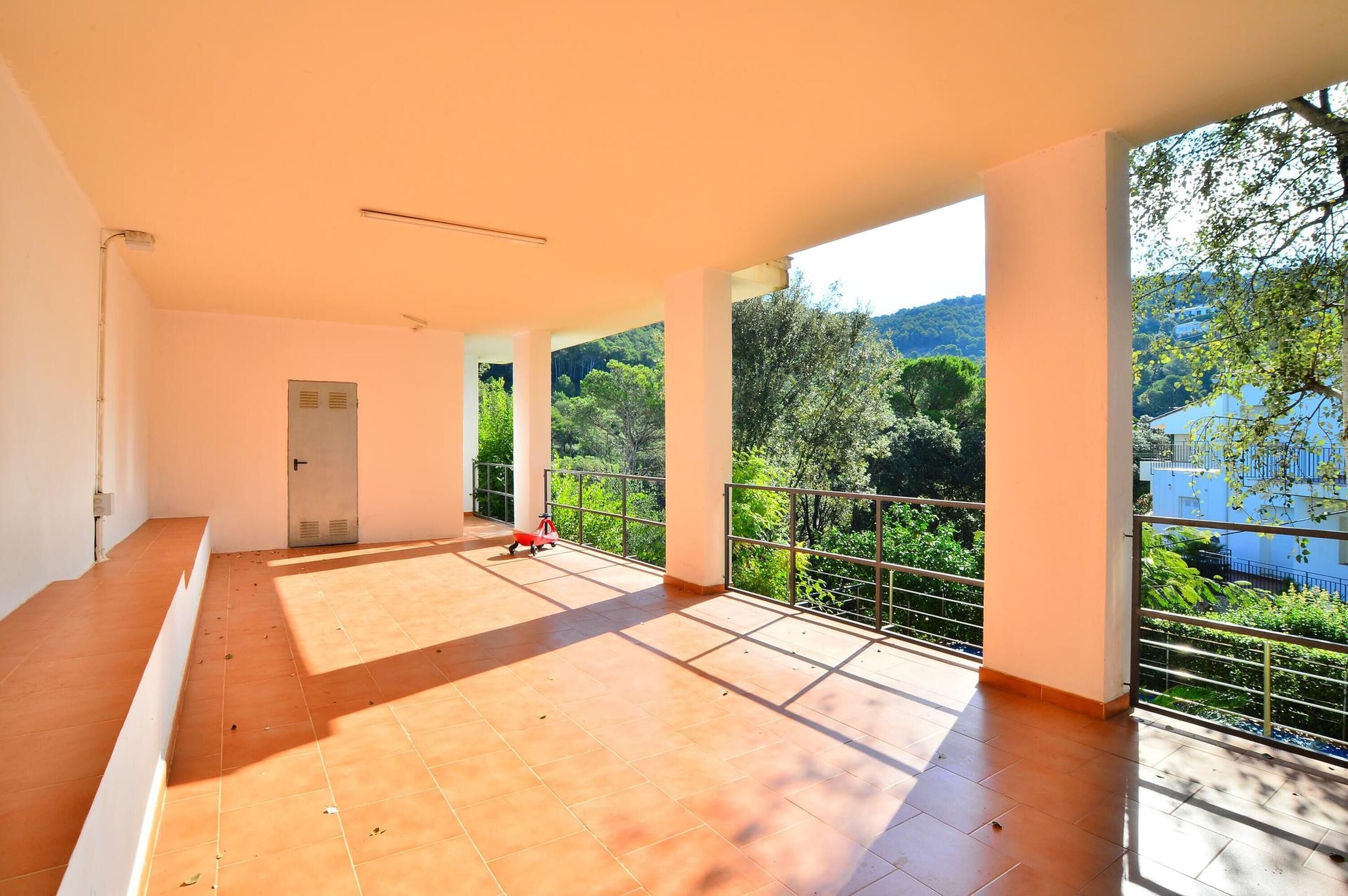 A spacious balcony with a tiled floor and a view of greenery and hills.