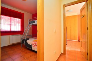 A room with a bunk bed, a radiator, a window with red curtains, and a wooden door. - Fantastic house with pool 600m from Sa Riera beach (Begur)