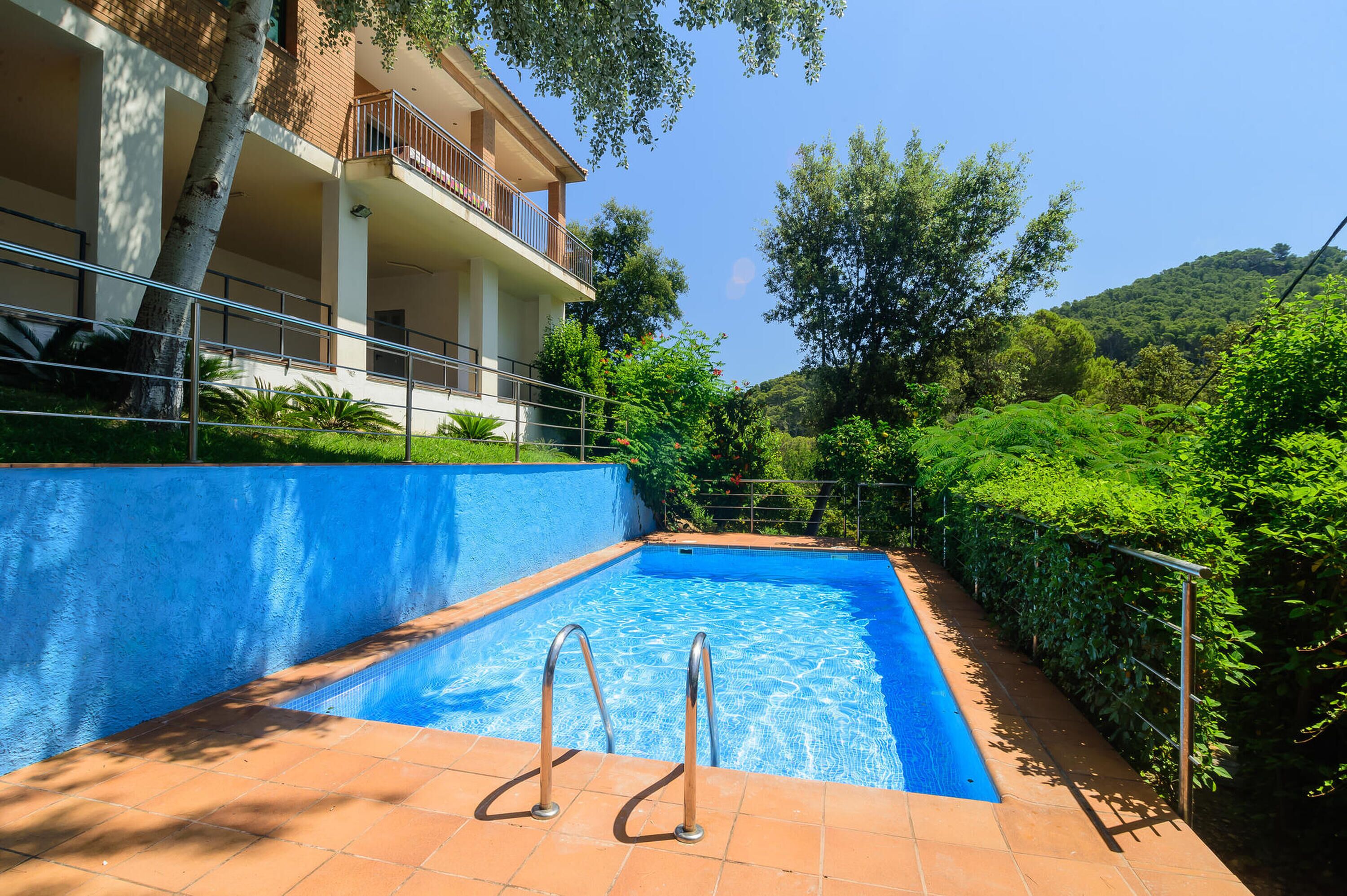 A swimming pool with metal railings, a tiled deck, and a building with balconies.