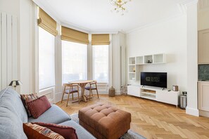A living room with a sofa, ottoman, TV, and dining table. - GuestReady - Modern Oasis in Kensington (London)