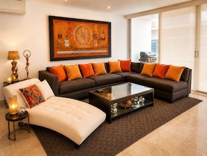 A modern living room with a sectional sofa, a glass coffee table, and a large framed artwork on the wall. - Deva - Artsy Playa Escape close to Quinta Ave (Playa del Carmen)