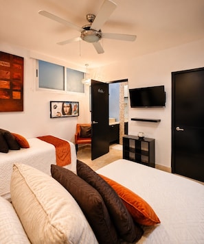 Ein Schlafzimmer mit zwei Betten, einem Deckenventilator, einem Fernseher und einer Tür zu einem Badezimmer.