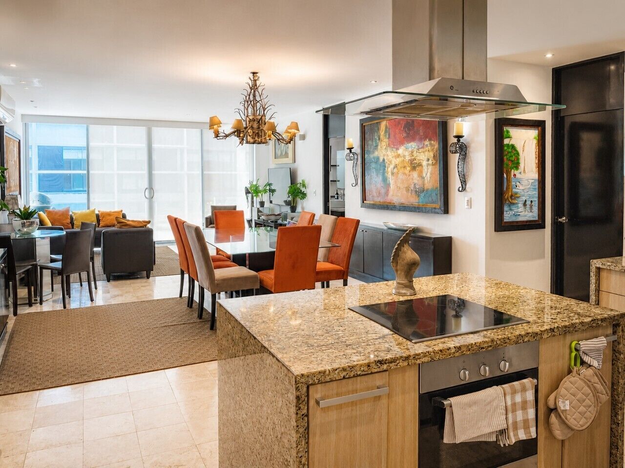 A modern kitchen with granite countertops, a built-in oven, and a dining area with orange chairs.