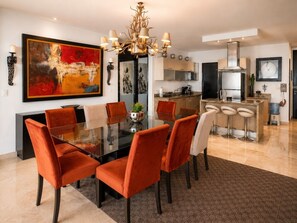 A modern dining area with a glass table, orange chairs, and a chandelier. - Deva - Artsy Playa Escape close to Quinta Ave (Playa del Carmen)