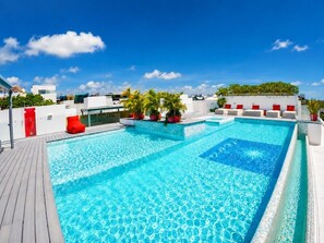 A rooftop swimming pool with a wooden deck, surrounded by potted plants and red seating. - Deva - Artsy Playa Escape close to Quinta Ave (Playa del Carmen)