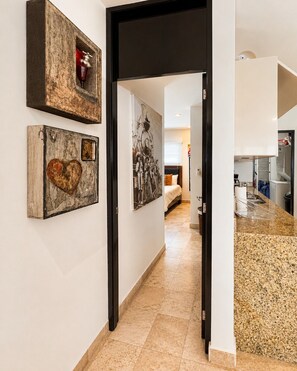 A hallway with artwork on the walls, a kitchen area visible through an open door, and a tiled floor. - Deva - Artsy Playa Escape close to Quinta Ave (Playa del Carmen)
