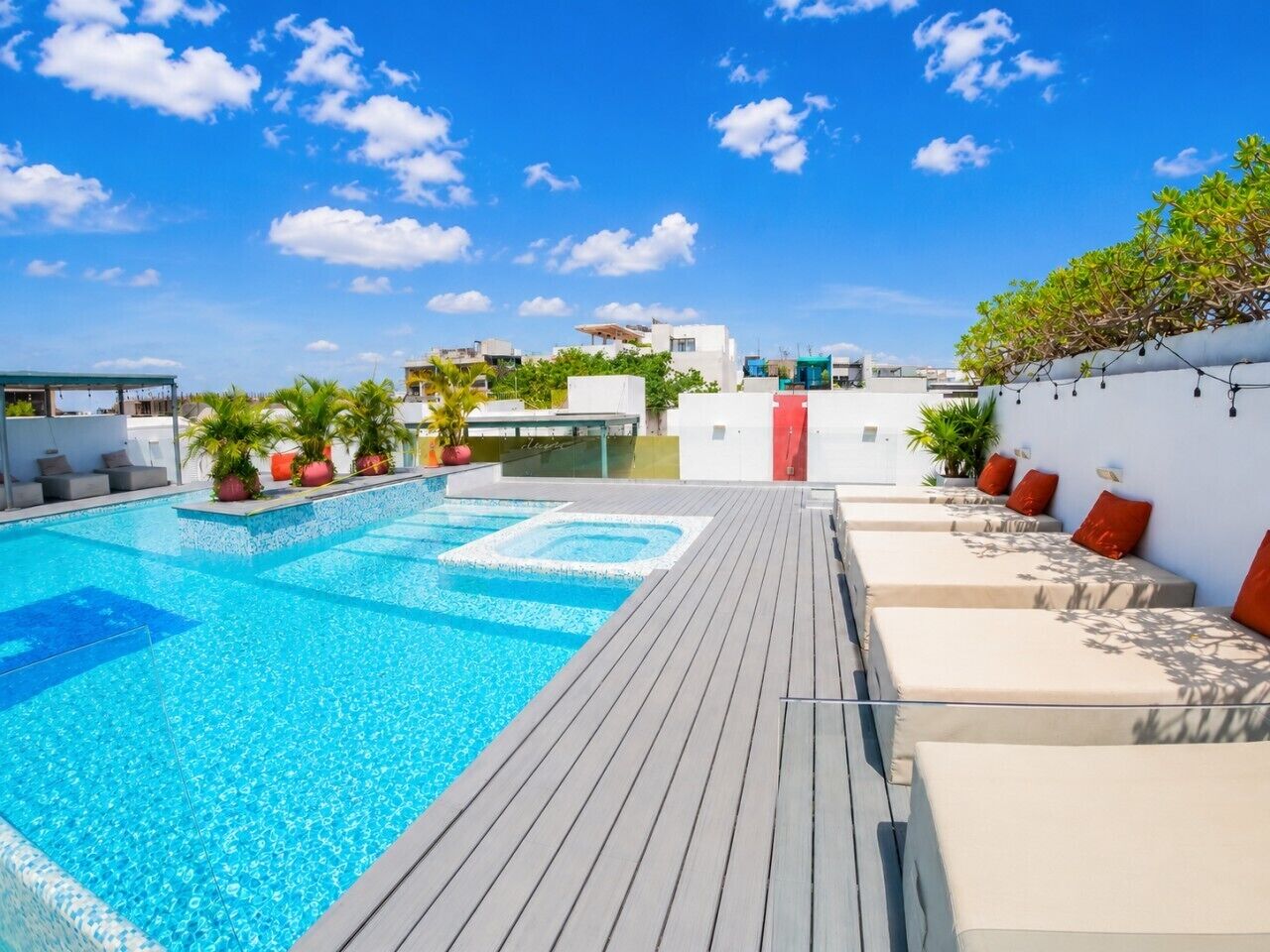 A rooftop swimming pool with a wooden deck, lounge chairs, and potted plants.