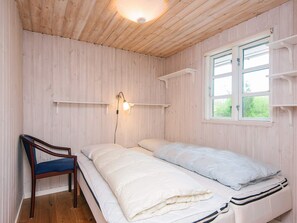 Ett rum med en säng, en stol, ett fönster och en hylla som är monterad på väggen.