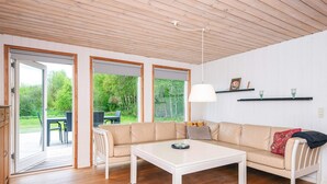 Ett modernt vardagsrum med en beige soffa, ett vitt soffbord och en matplats med ett bord och stolar. Stora fönster ger utsikt över omgivningen.