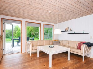 Ein modernes Wohnzimmer mit einem beigefarbenen Sofa, einem weißen Couchtisch und einem Essbereich mit Tisch und Stühlen. Große Fenster bieten Blick ins Freie.