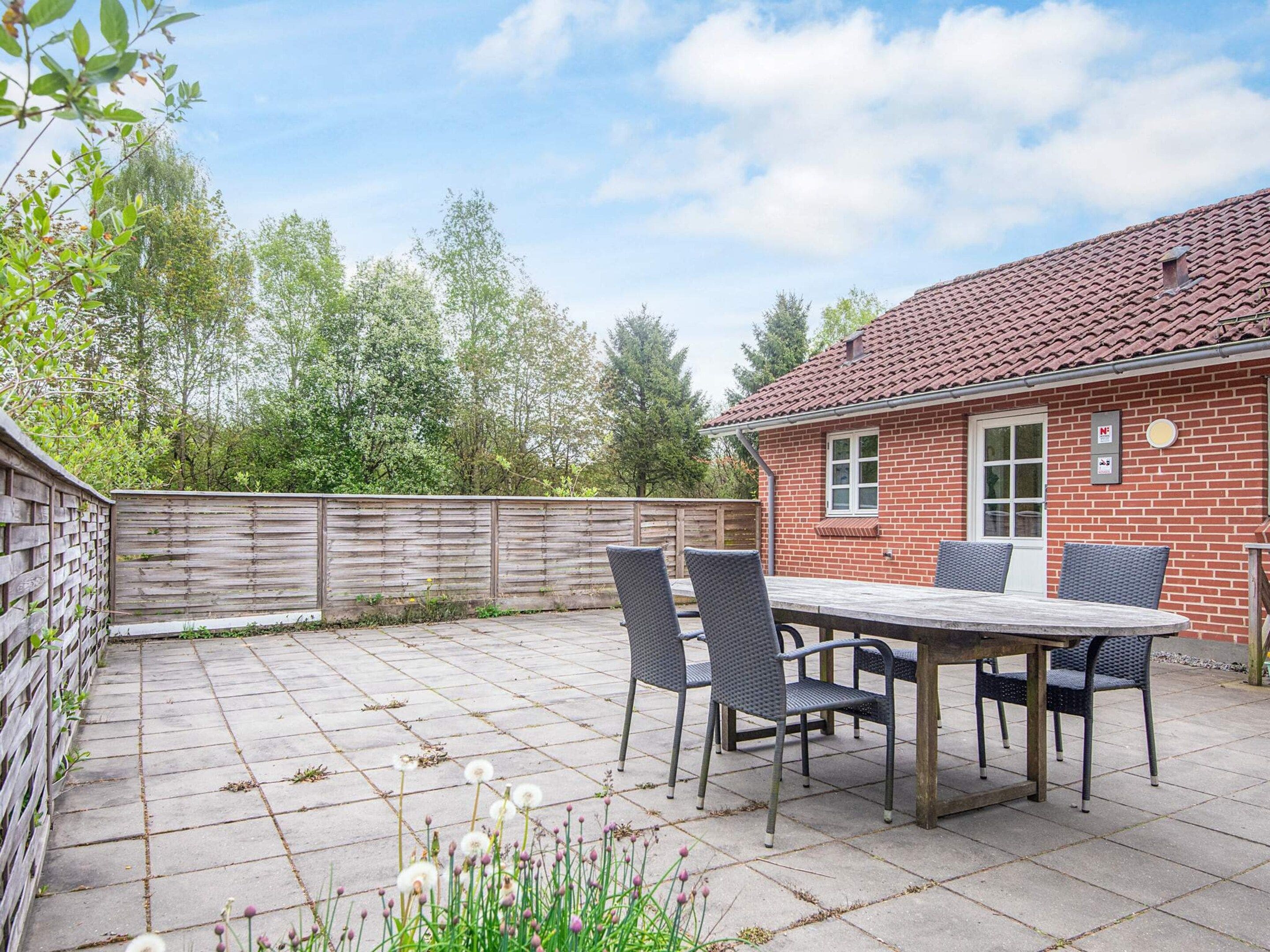 A patio with a table and chairs, a brick building, and a wooden fence.