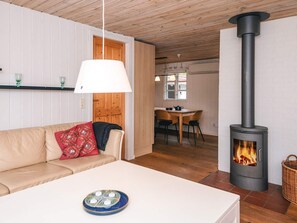 A cozy living room with a sofa, a table with a decorative plate, a fireplace, and a dining area with chairs and a table. - 5 Person Holiday Home in Herning (Herning)