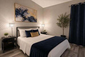 Ein Schlafzimmer mit einem Bett, zwei Nachttischen, einer Stehlampe und einem großen abstrakten Gemälde.
