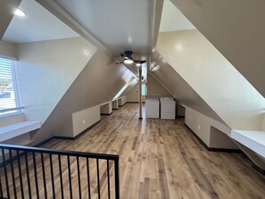Ein geräumiger Dachbodenraum mit schrägen Wänden, Holzdielenboden, fest eingebauten Bänken entlang der Wände und einem Deckenventilator.