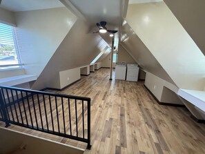 A spacious attic room with a wooden floor, a black railing, and a ceiling fan.