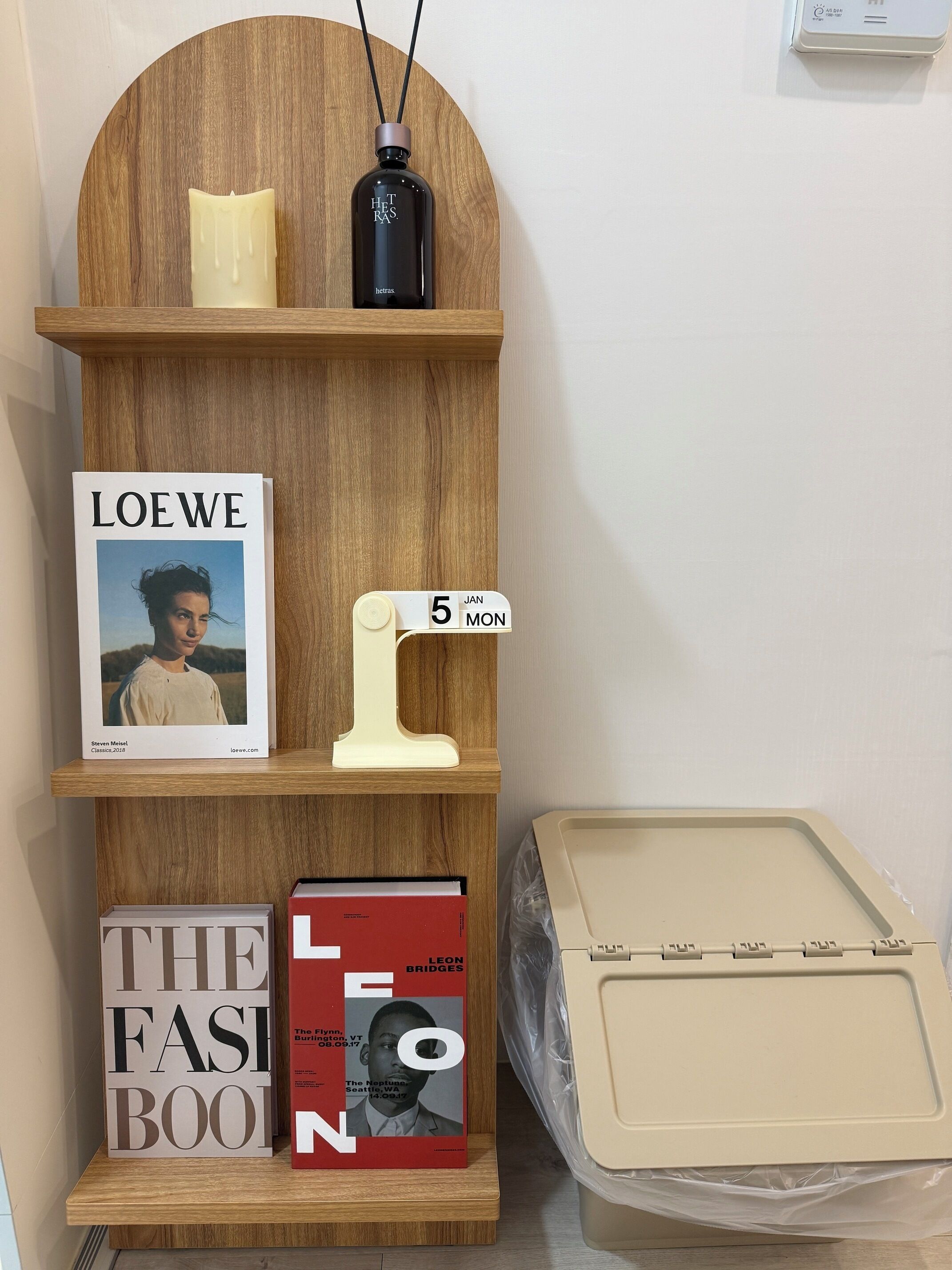 A wooden shelf with books, a candle, and a black bottle.