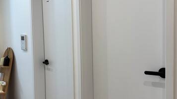 Un pasillo con dos puertas cerradas, un pequeño cesto de basura y un interruptor de luz en la pared.