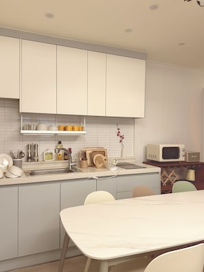 A modern kitchen with white cabinets, a sink, and a dining area with a table and chairs. - Esanghan Stay Suwon Ingye (Suwon)