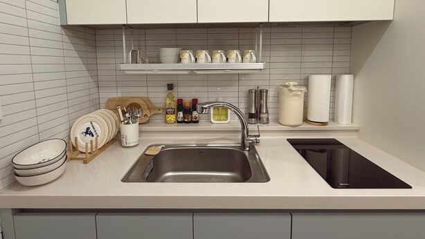 A modern kitchen with a stainless steel sink, white cabinets, and a countertop with various kitchen items.