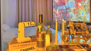 A hotel room with a bed, a table with a bottle, candles, a wine glass, and a projector screen displaying a Christmas tree.