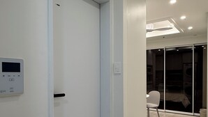 A modern interior with a closed door, a control panel, and a glimpse of a kitchen area with a chair. - Esanghan Stay Suwon Ingye (Suwon)