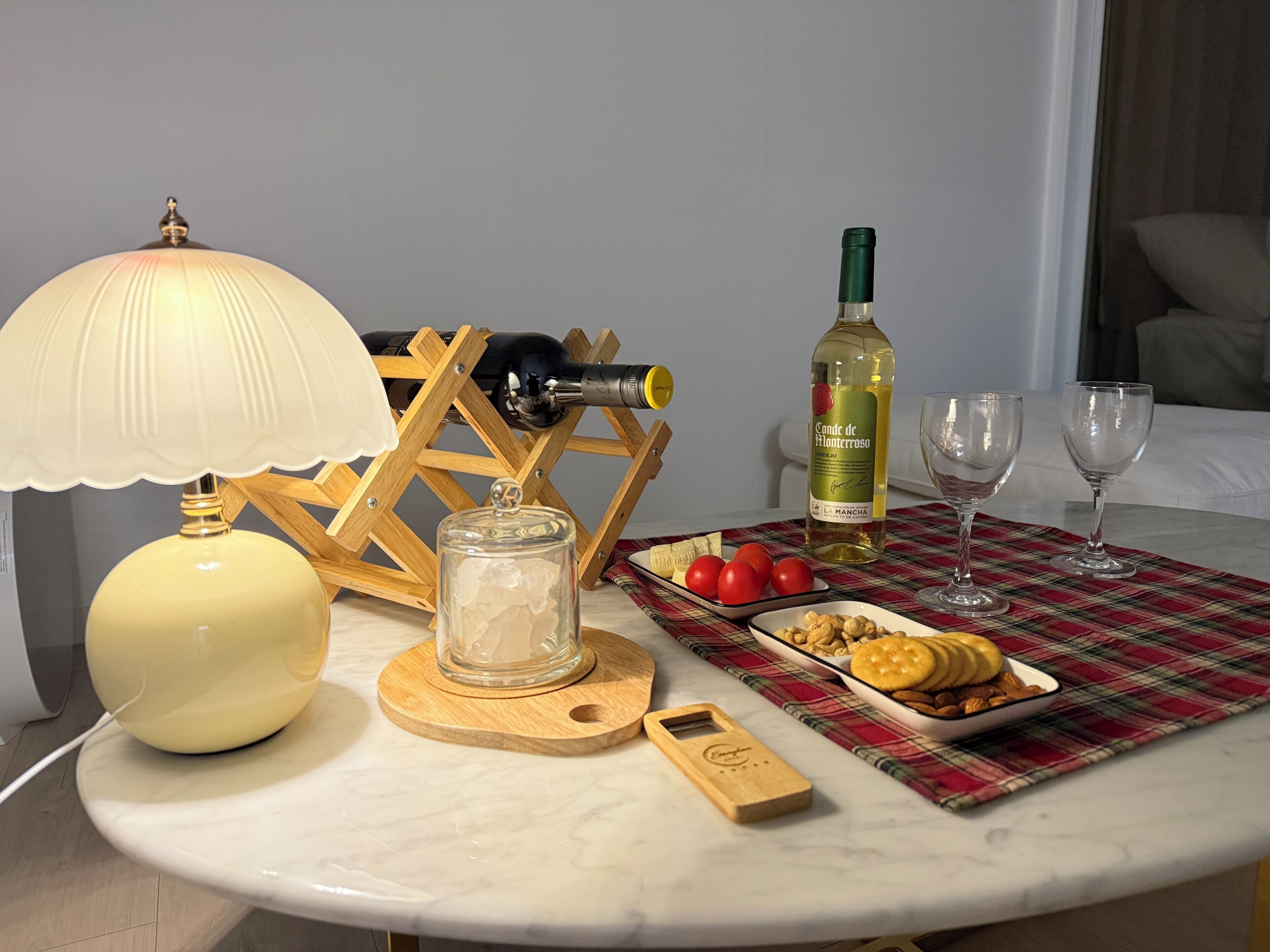 A table with a bottle of wine, glasses, a lamp, a jar, and a plate with snacks.