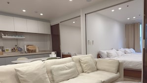 A modern hotel room with a sofa, a round marble table, a bed, and a kitchen area.